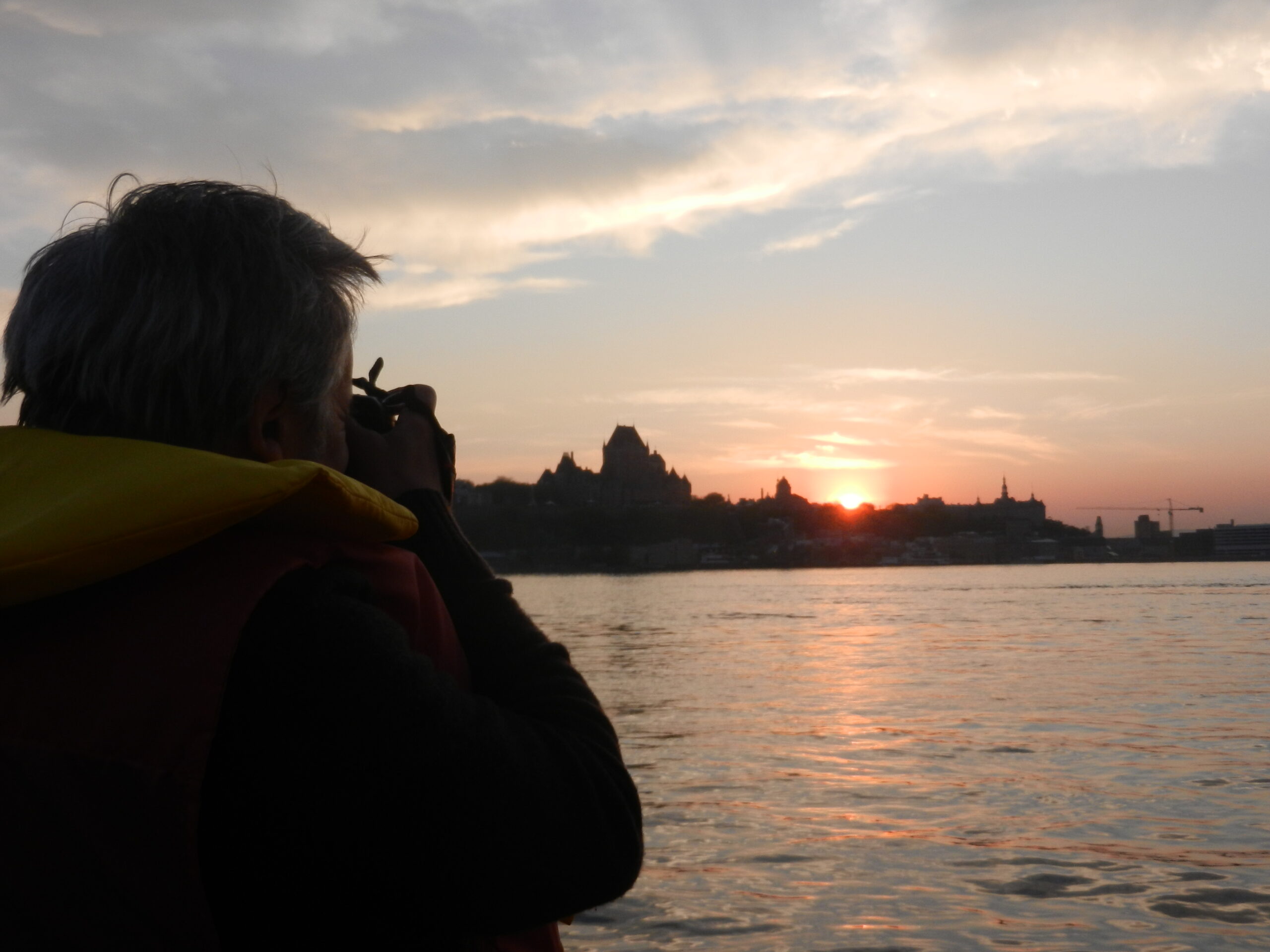 Homme portant une veste de flottaison à bord d'un bateau d'Excursions Maritimes Québec, photographiant le Château Frontenac.